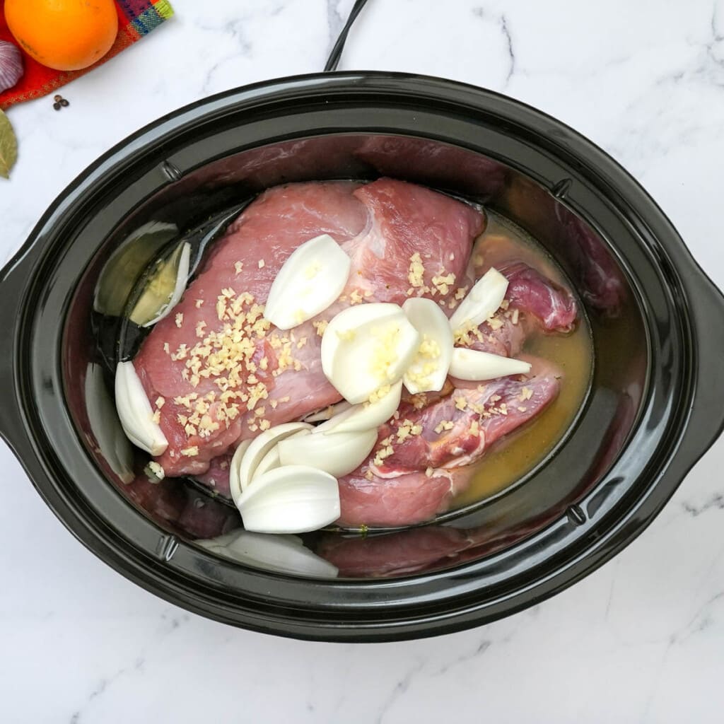 Adding onions and garlic to pork carnitas in slow cooker.