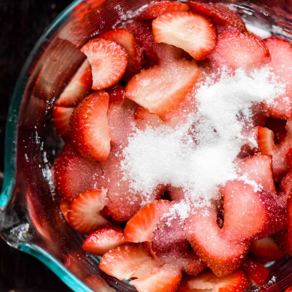 Strawberries and granulated sugar in glass bowl.