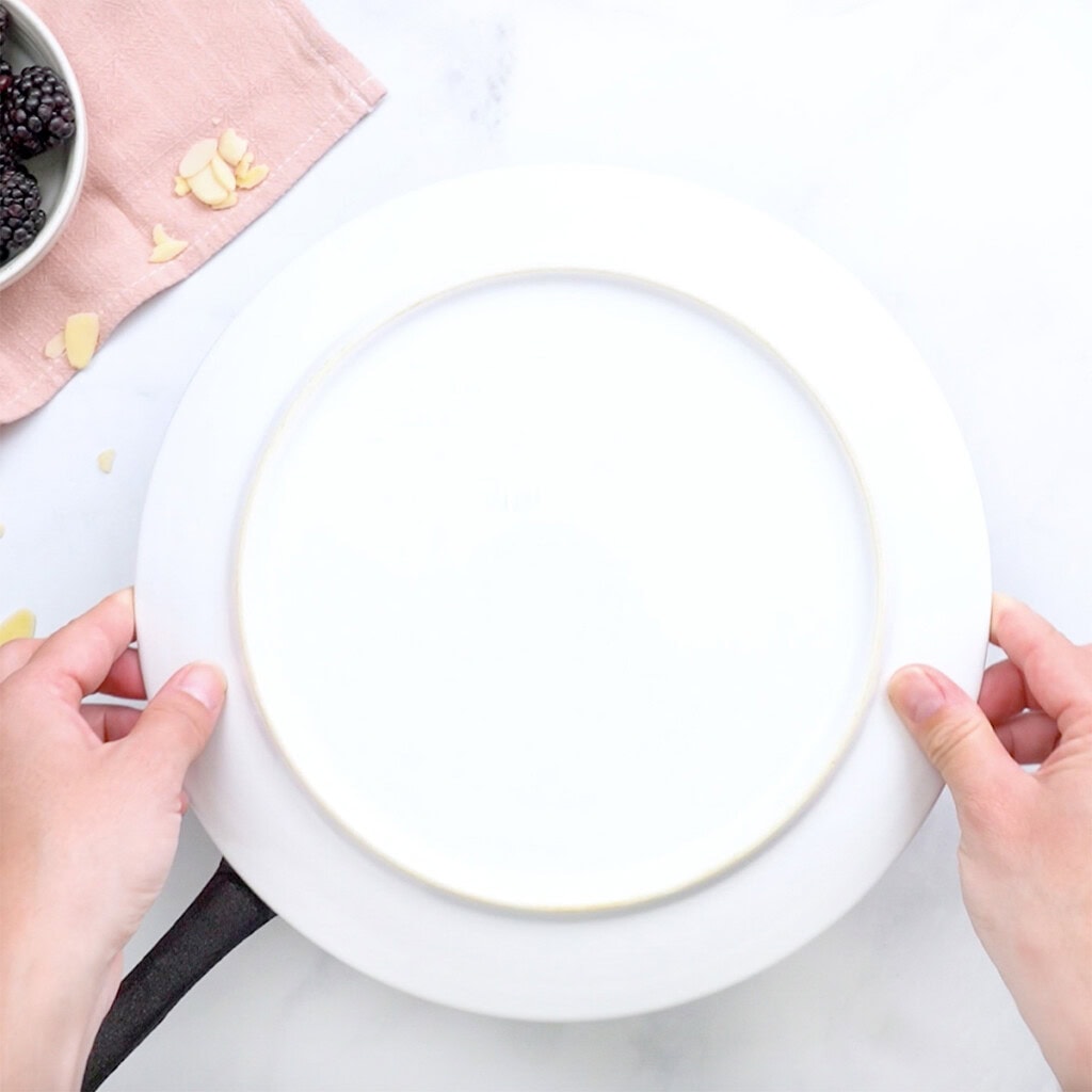 Placing plate over skillet to overturn cake.