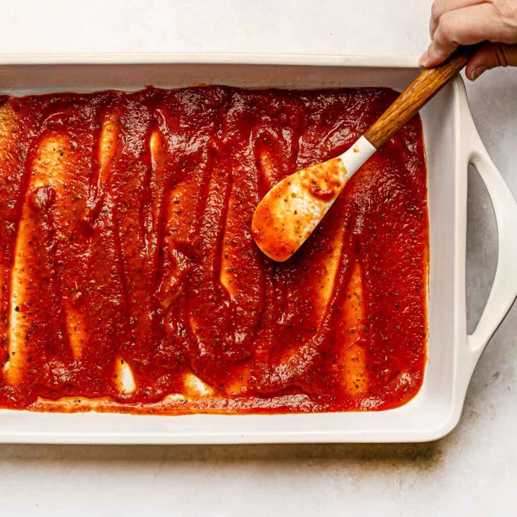 Adding sauce to bottom of dish for Stuffed Shells with Meat.