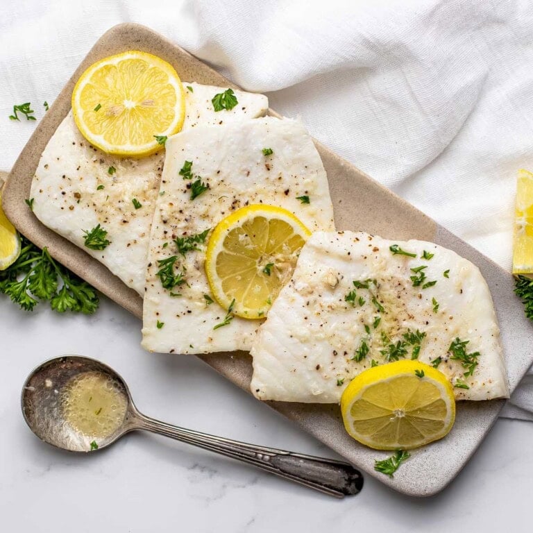 Baked Halibut on platter with lemon garlic butter, fresh lemons, and parsley garnish.