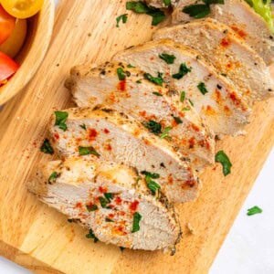 Mediterranean Chicken Marinade sliced chicken on cutting board with parsley garnish.