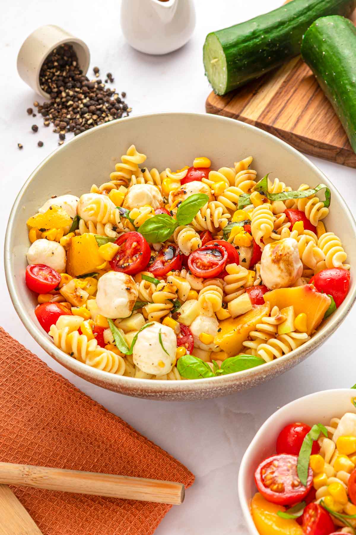 Summer Pasta Salad recipe on table with cucumber, black peppercorns, and more.