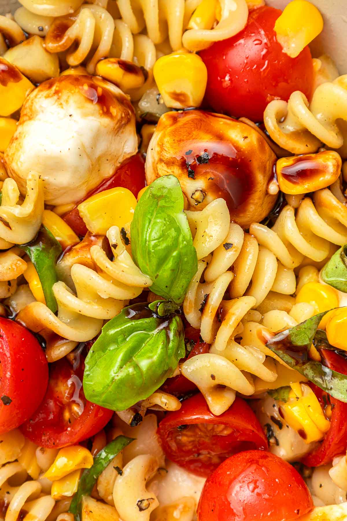 Summer Pasta Salad close-up showing pasta, tomatoes, corn, cucumber, nectarines, fresh mozzarella, and fresh basil.