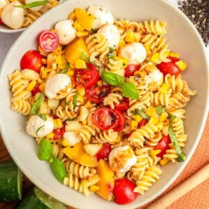 Summer Pasta Salad in bowl with corn, tomatoes, nectarines, cucumber, fresh mozzarella, fresh basil, and white balsamic vinaigrette.