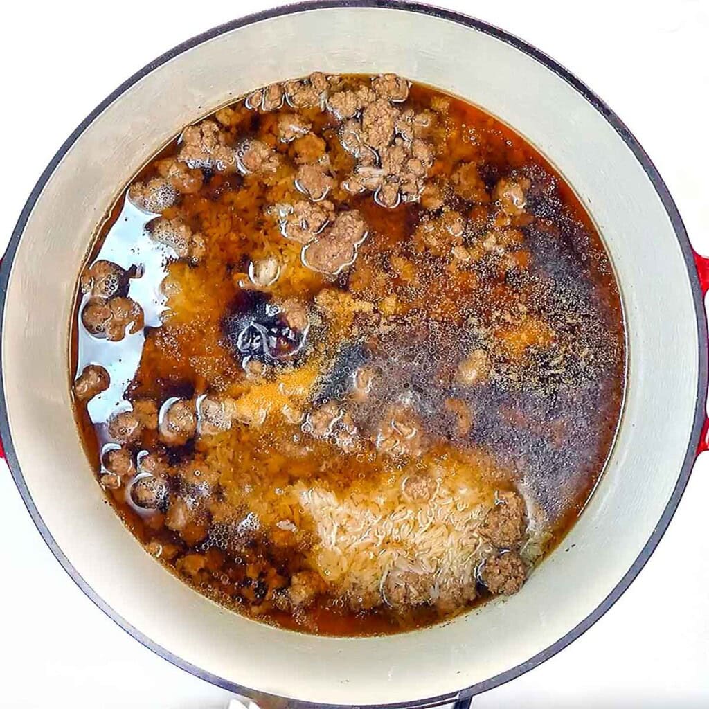 Adding broth and other ingredients to pot for ground beef and rice recipes.