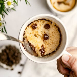Chocolate Chip Mug Cake in mug with spoon held in hand.