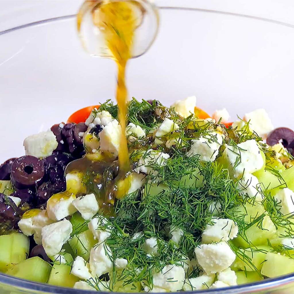 Pouring vinaigrette over tomato cucumber feta salad.