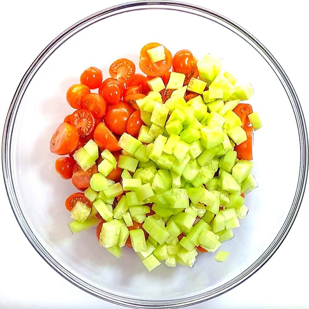 Adding cucumbers to bowl for tomato and cucumber and feta salad.