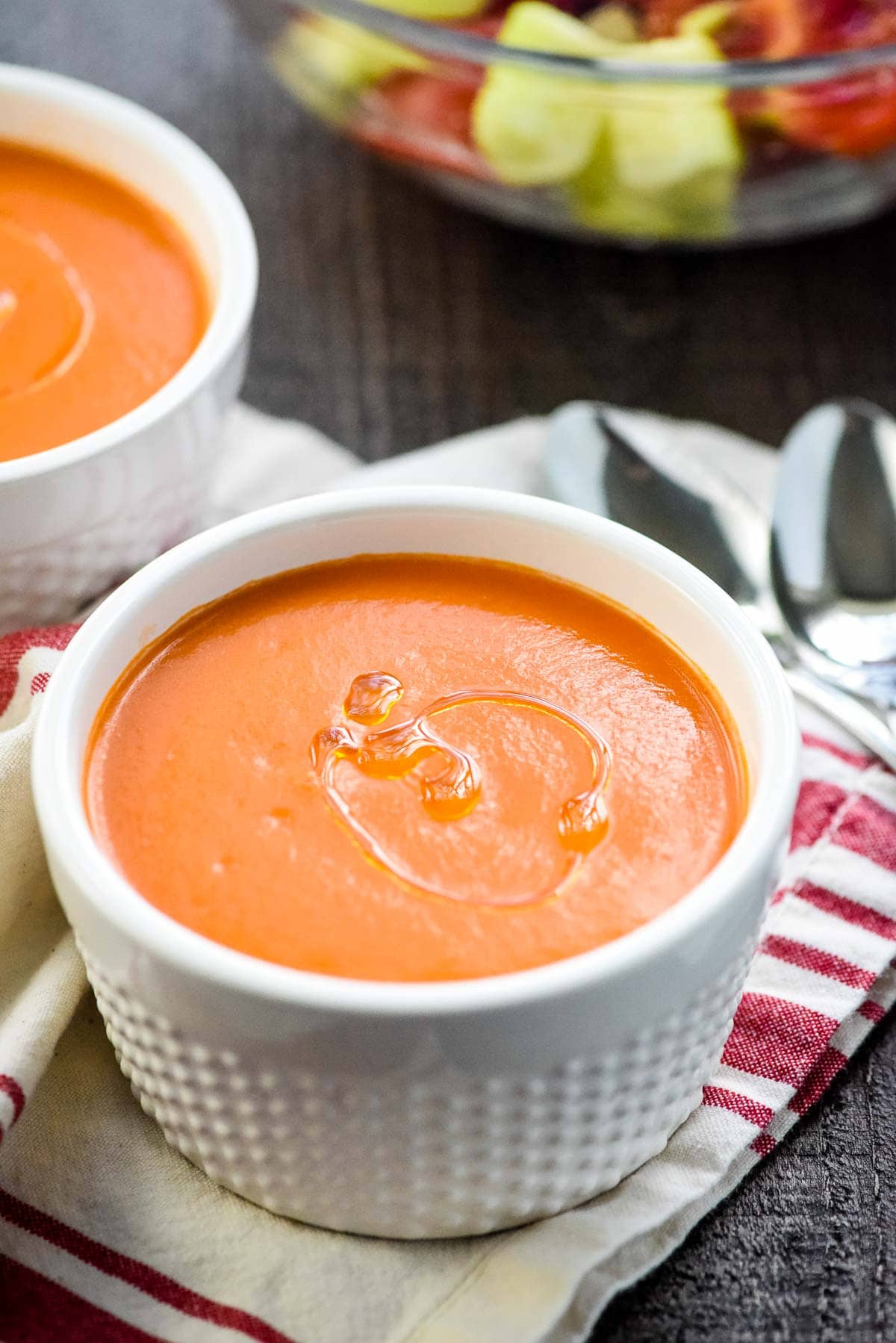 Gazpacho in bowls with cucumber and tomatoes in background.
