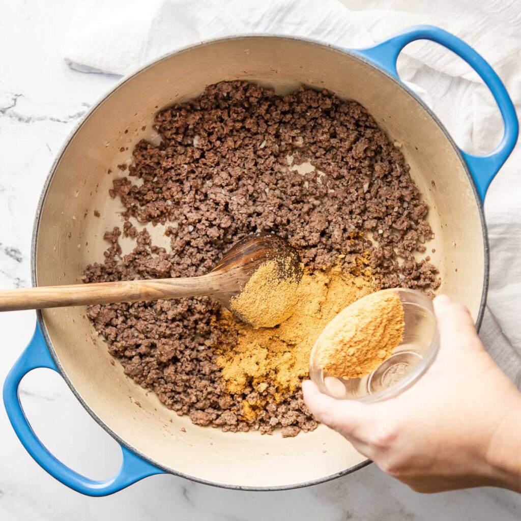 Adding taco seasoning to beef for Beef and Bean Burritos.