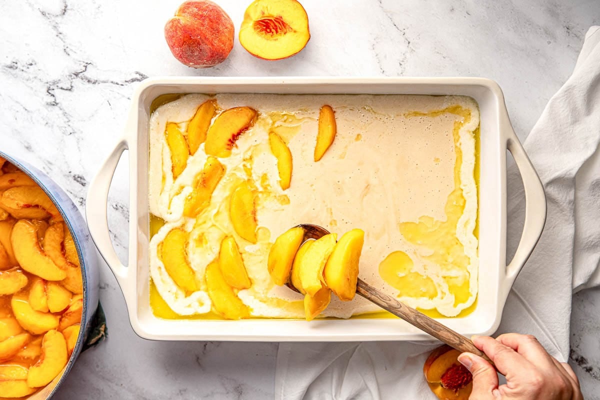 Spooning peaches over batter for southern peach cobbler recipe.