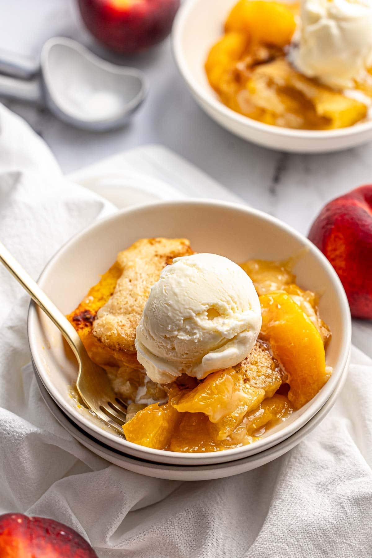 Easy Peach Cobbler in two bowls with vanilla ice cream.