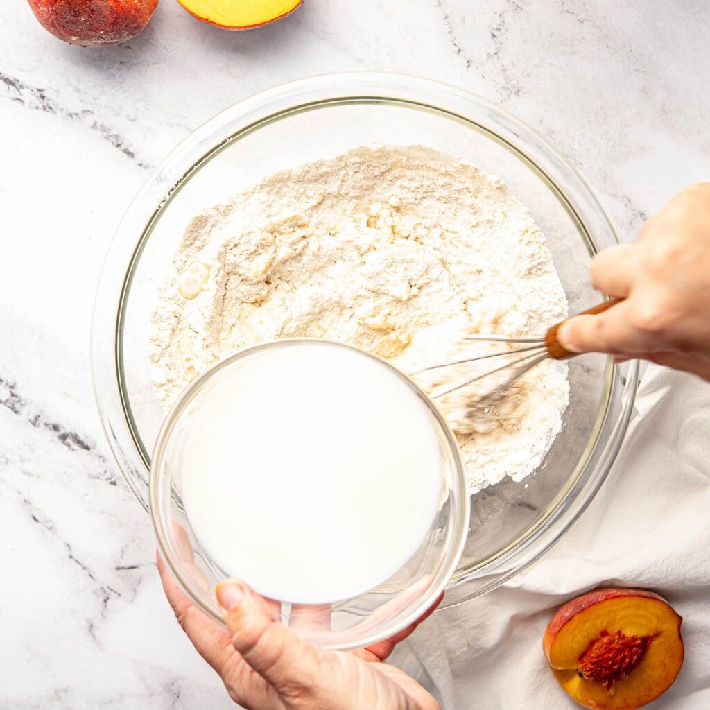 Adding milk to dry ingredients for southern peach cobbler recipe.