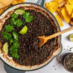 Seasoned Black Beans aerial view in pan with serving spoon and garnishes.