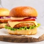 Chicken Burger Recipe on wooden board with cheese, lettuce, tomato, onion, and burger sauce.