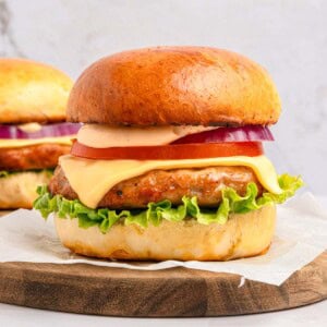 Chicken Burger Recipe on wooden board with cheese, lettuce, tomato, onion, and burger sauce.