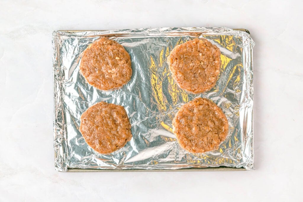 Chicken burger patties on baking sheet.