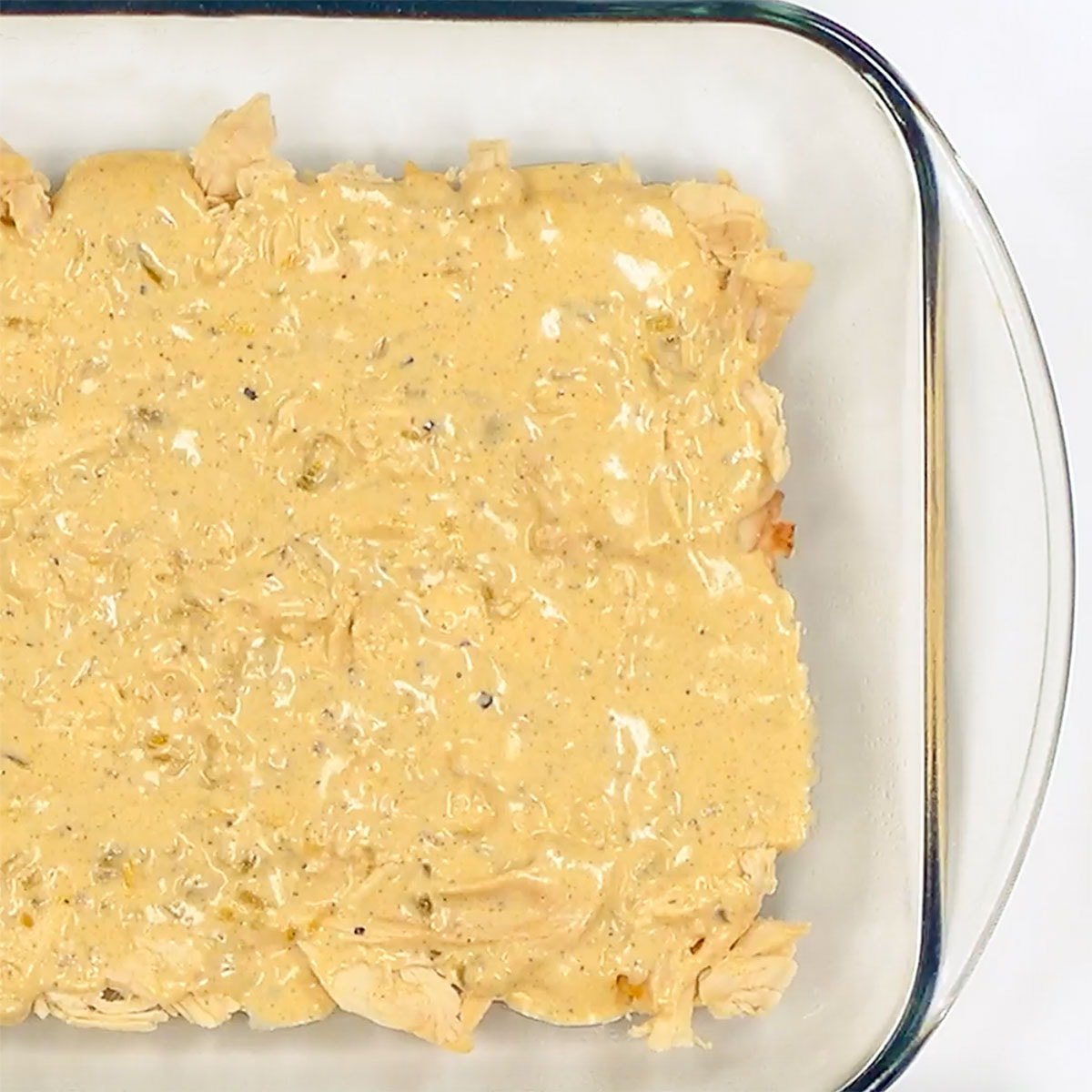 Layering sauce on top of chicken for Chicken Enchilada Casserole recipe.