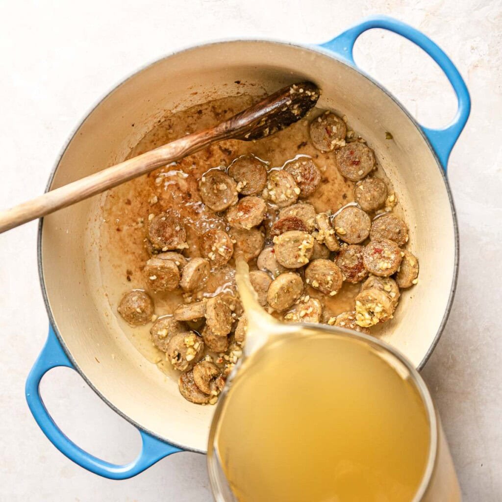 Pouring broth into Chicken Sausage Pasta recipe.