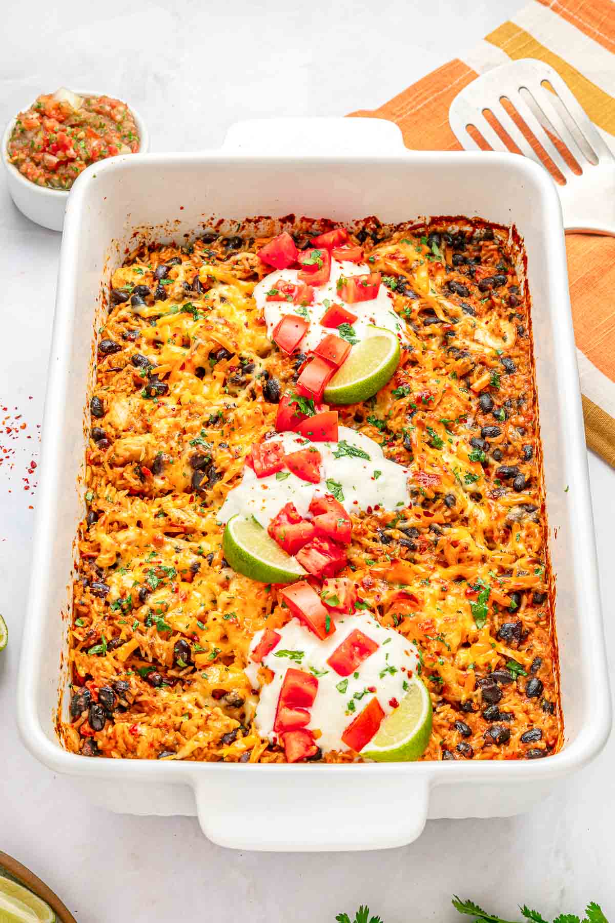 Mexican Chicken and Rice Casserole topped with sour cream, tomatoes, cilantro, and lime wedges.