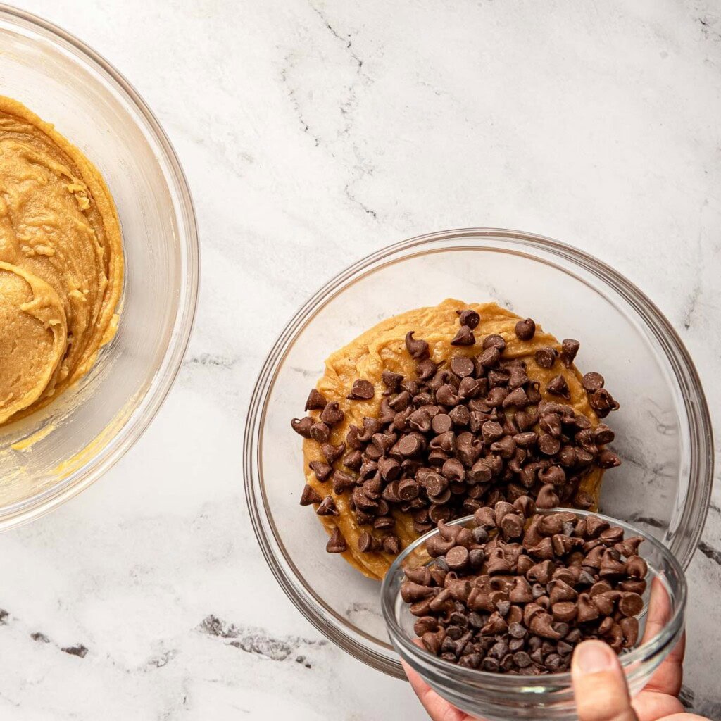Adding chocolate chips to one bowl for chocolate chip cookie layer.