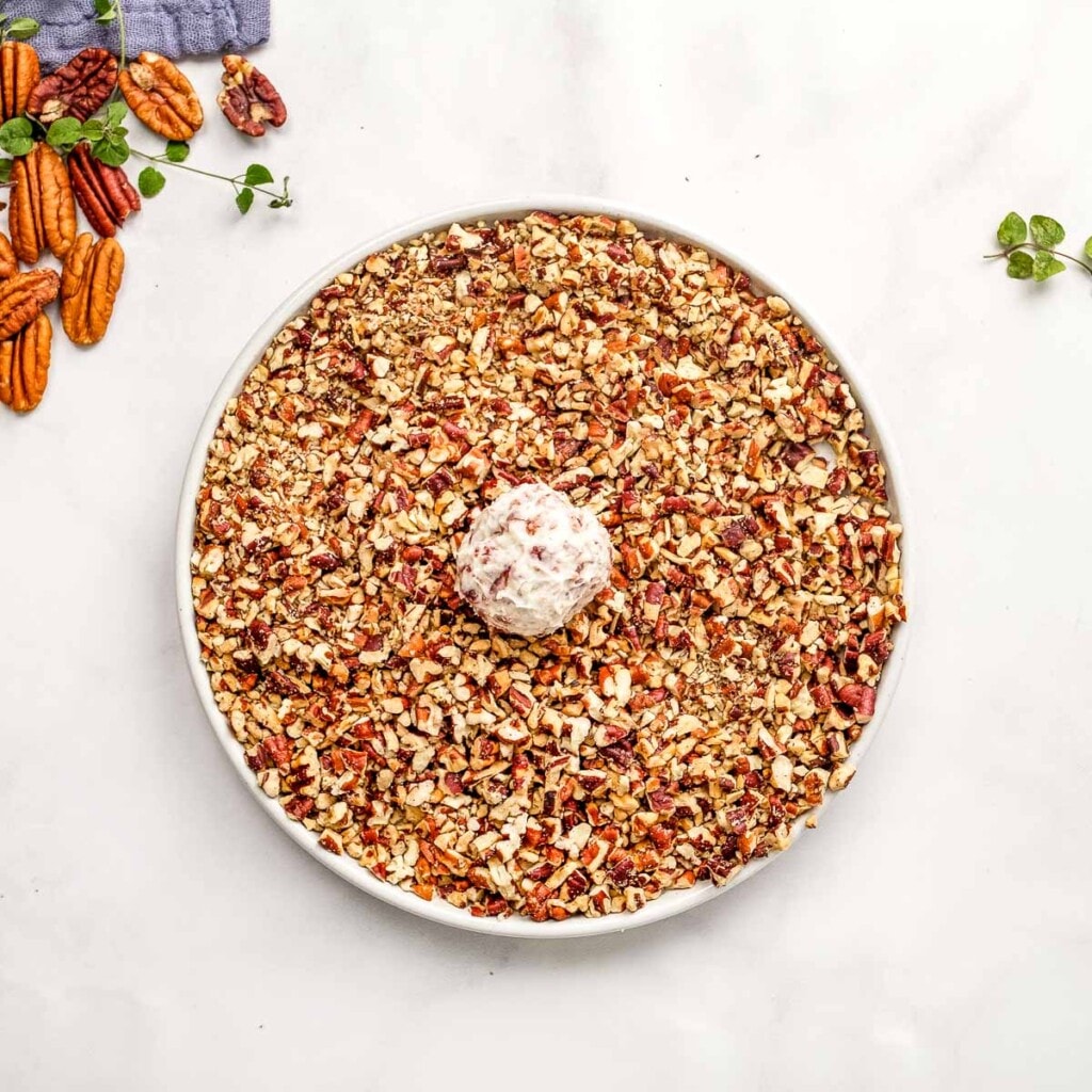 Rolling Mini Cheese Balls in chopped pecans.