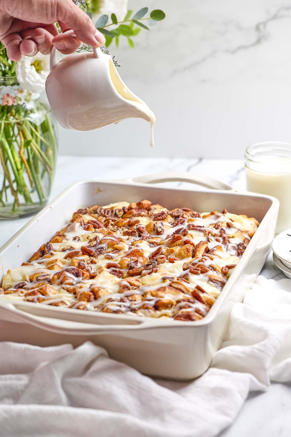 Cinnamon Roll Casserole with icing being poured over.