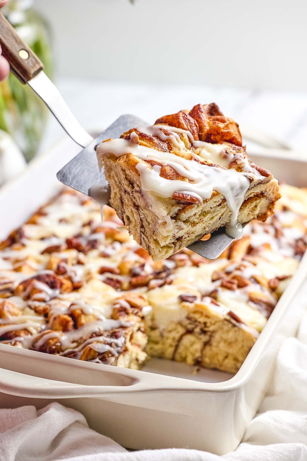 Cinnamon Roll Casserole slice held over baking dish.