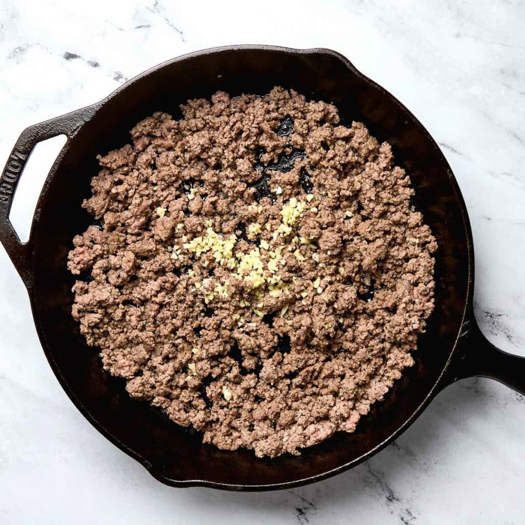 Browned ground beef in skillet with garlic for cowboy tater tot casserole.