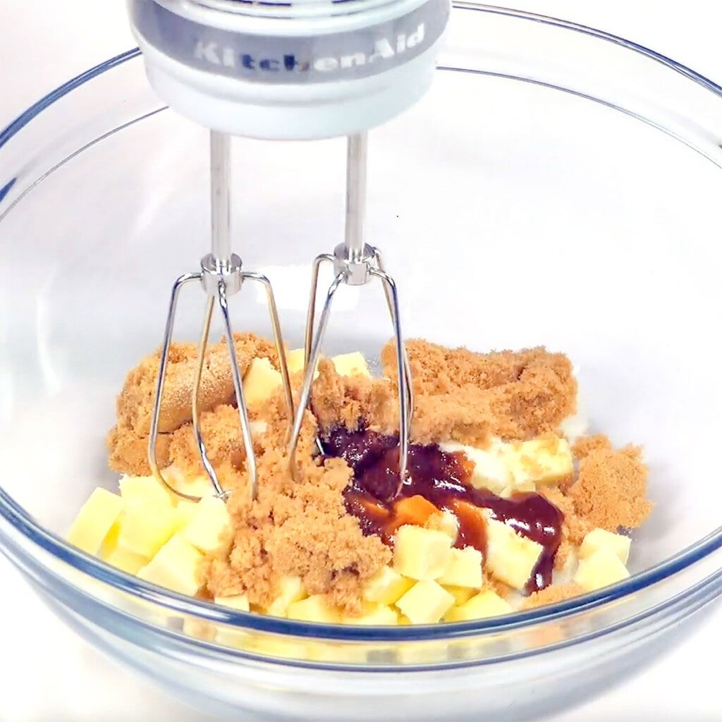 Blending butter with sugars using electric mixer.